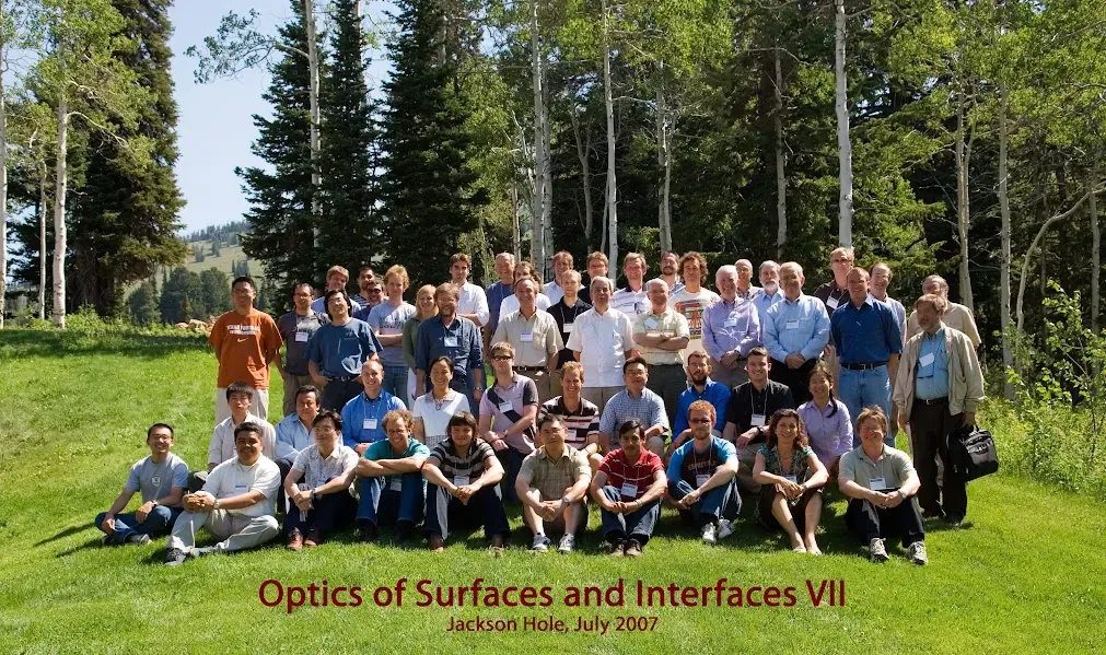 Foto de grupo de unos sesenta participantes sobre el pasto, con bosque al fondo, en el congreso Optics of Surfaces and Interfaces VII.